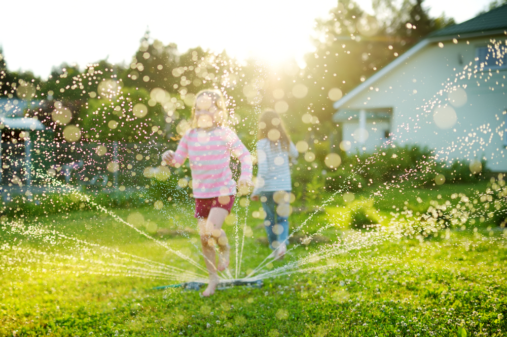 Little girls running through a sprinkler in the backyard