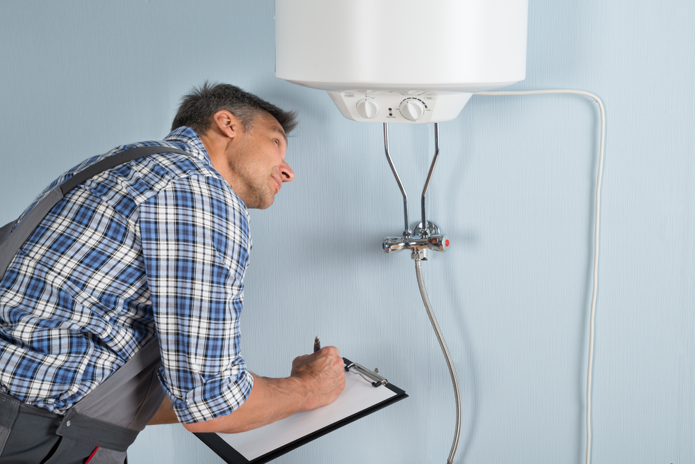 Male plumber holding a clipboard looking at an electric boiler
