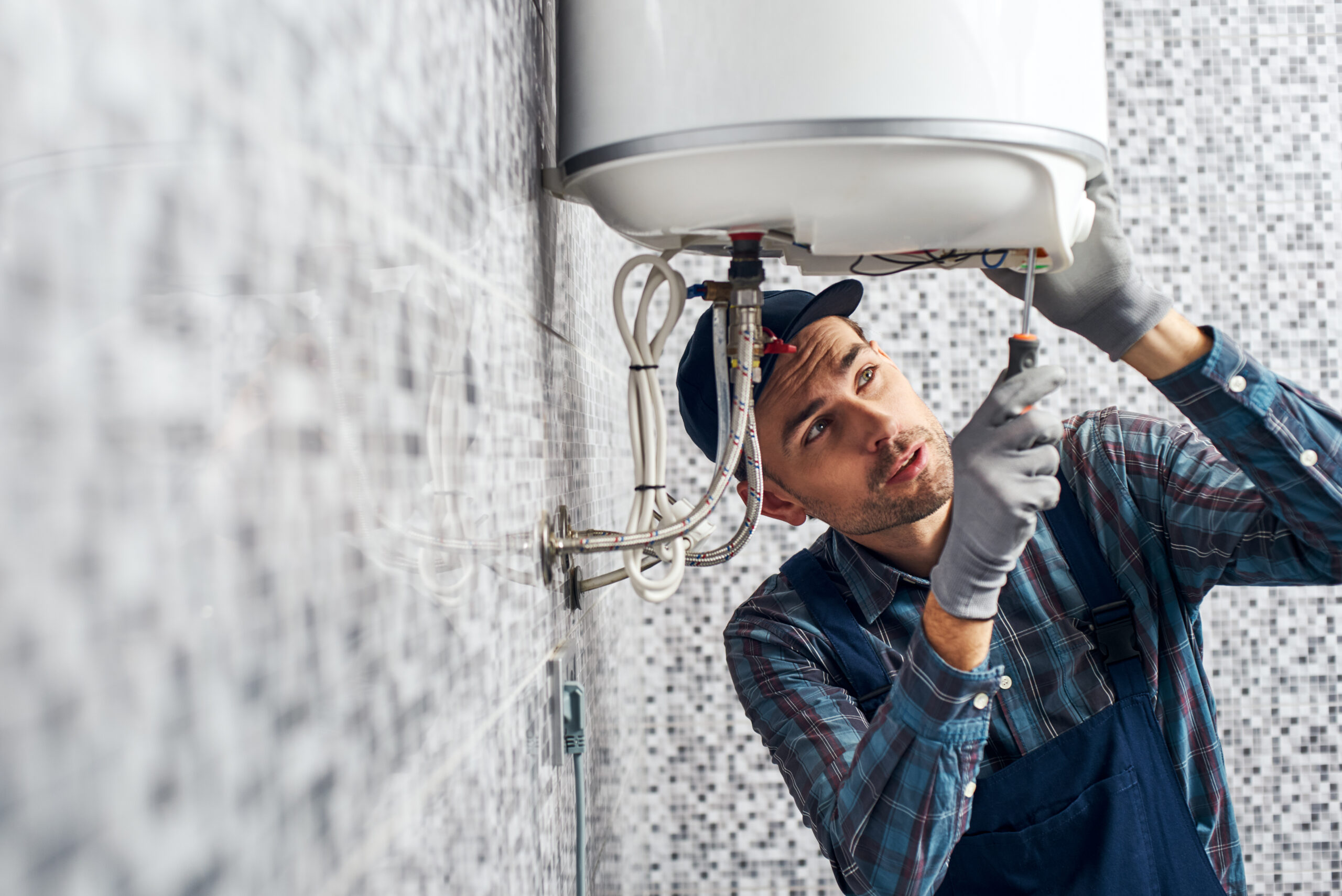 A plumber working on a hot water system with a screwdriver