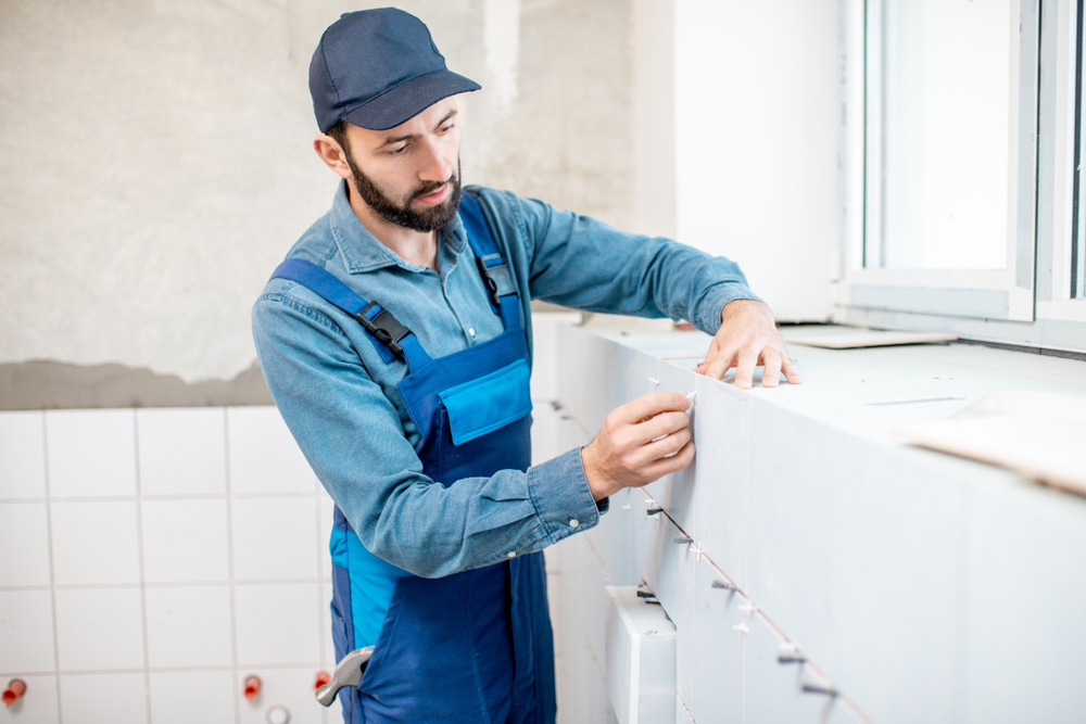 Tiler installing white ceramic bathroom tiles